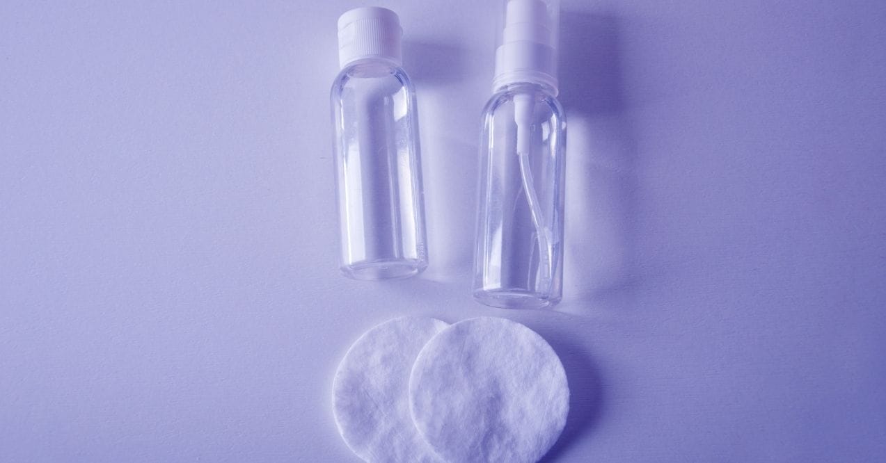 Two clear toner bottles with cotton pads on violet background