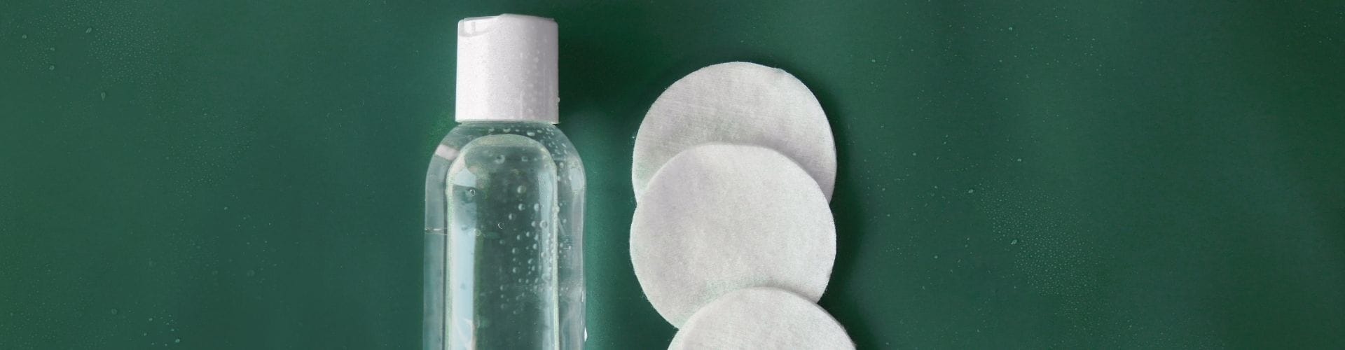 Clear bottle of facial toner with cotton pads on green background