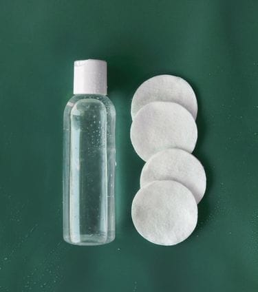 Clear bottle of facial toner with cotton pads on green background