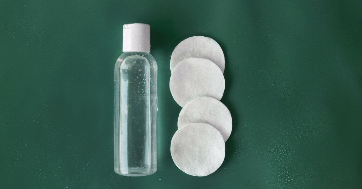 Clear bottle of facial toner with cotton pads on green background