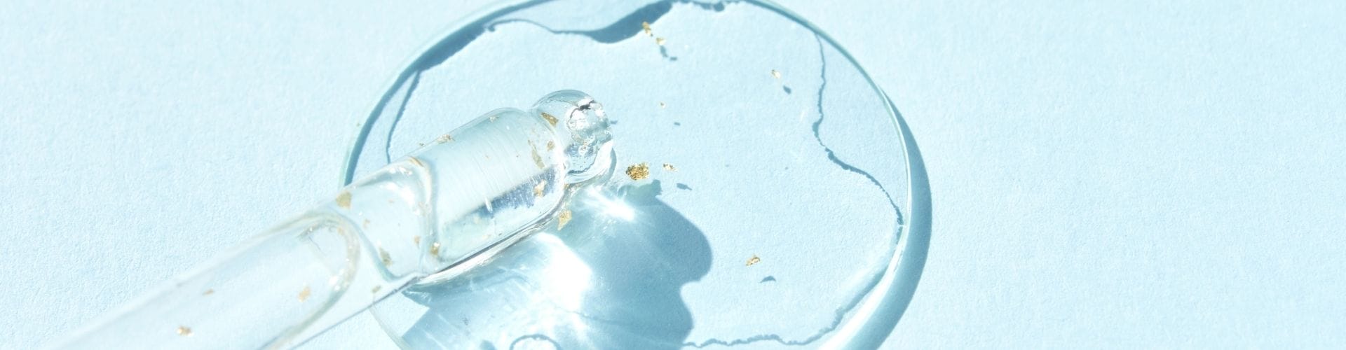 Clear serum with gold flecks in a dropper on a blue background