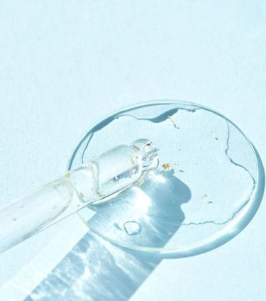 Clear serum with gold flecks in a dropper on a blue background