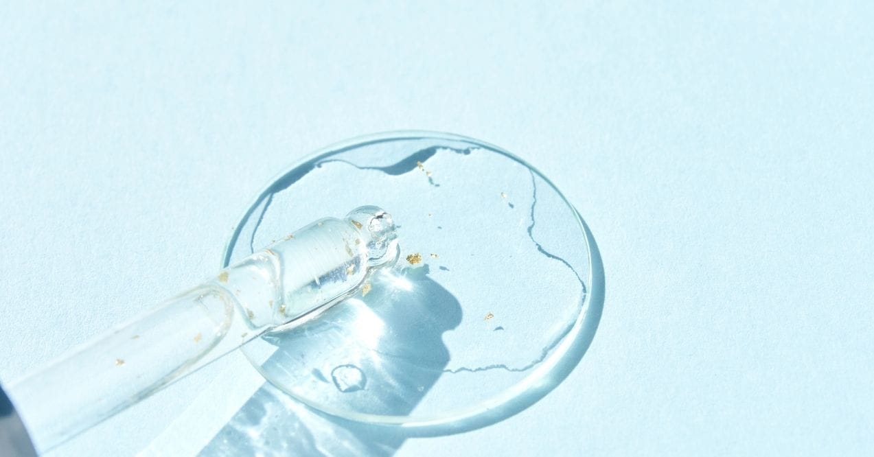 Clear serum with gold flecks in a dropper on a blue background