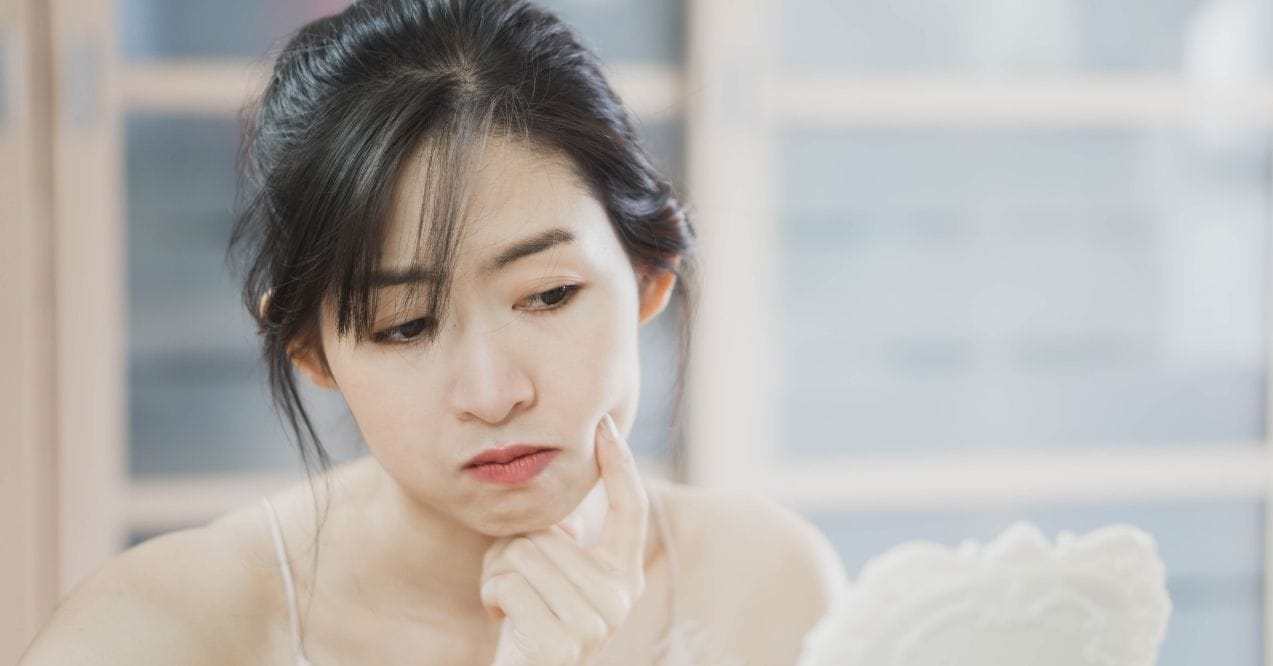 Woman looking at her face in a mirror with concern about oily skin