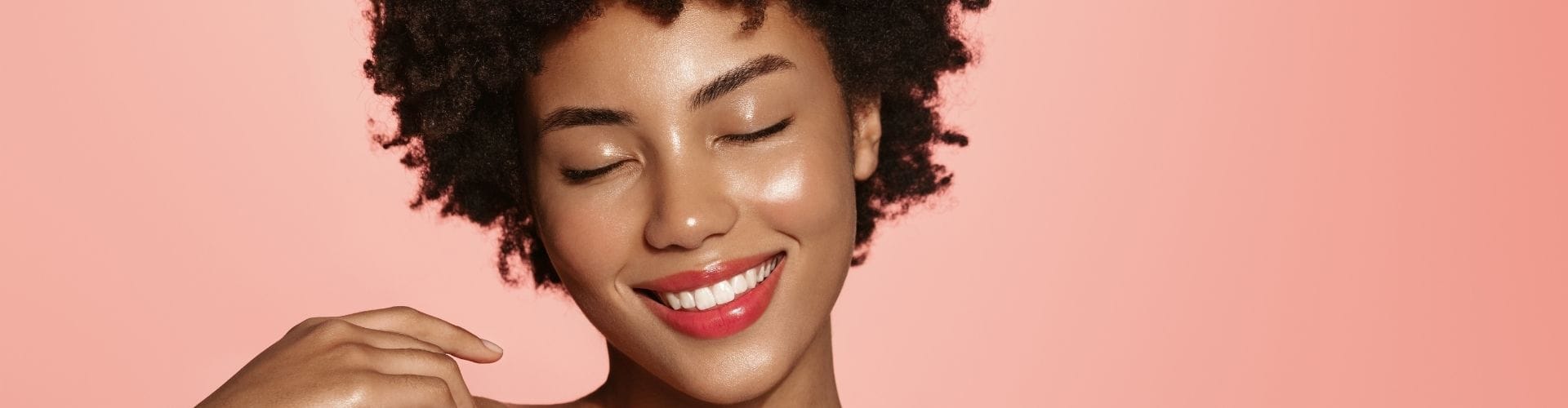 Smiling woman with shiny, glowing skin against a peach background