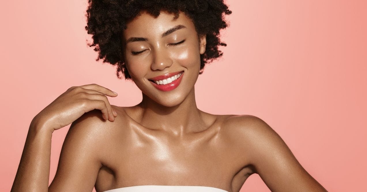 Smiling woman with shiny, glowing skin against a peach background