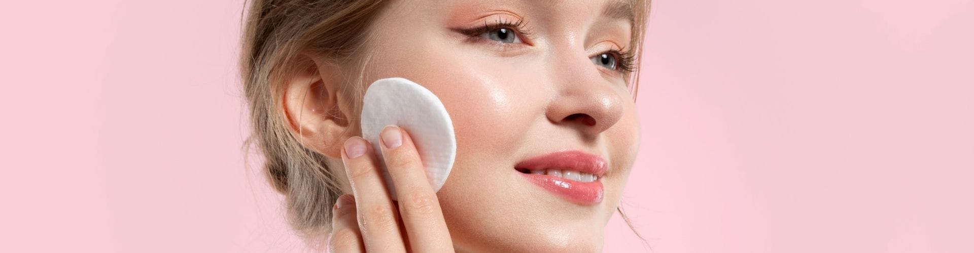 Woman with radiant, glowy skin using a cotton pad on her cheek