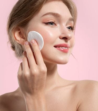 Woman with radiant, glowy skin using a cotton pad on her cheek