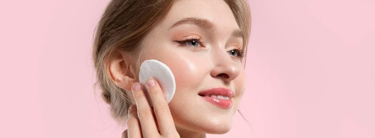 Woman with radiant, glowy skin using a cotton pad on her cheek