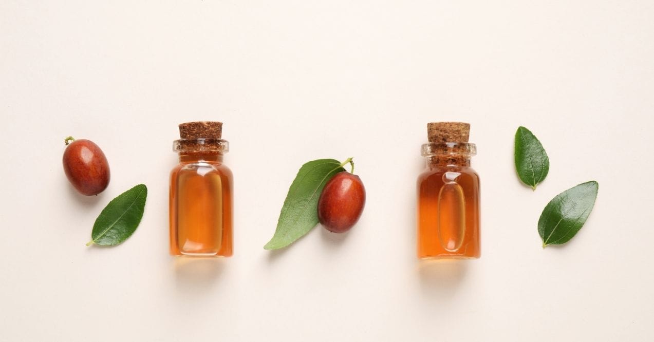Jojoba oil bottles with seeds and leaves on light background